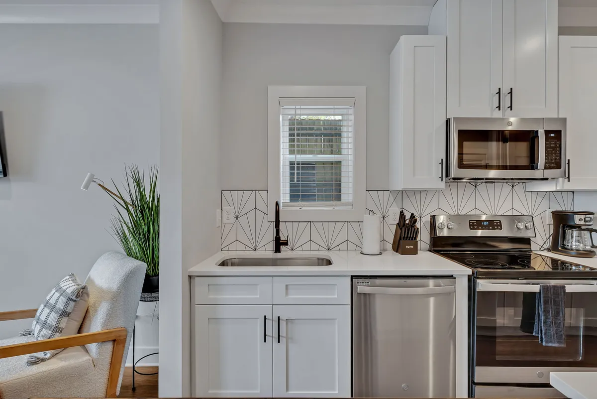 A modern kitchen and adjacent cozy seating area are highlighted, featuring sleek appliances, a geometric tile backsplash, and an inviting spot for guests to relax or socialize. The design suggests both comfort and urban sophistication.