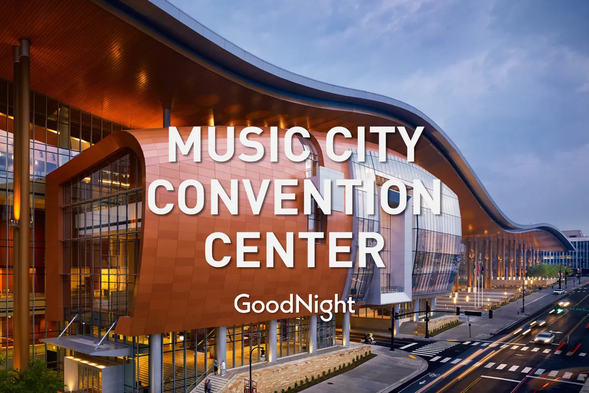 This image showcases the iconic, curved roof and large glass windows of the Music City Convention Center, with the building's warm façade bathed in inviting light. The shot captures the energy and scale of this major business hub, hinting at the lively activity inside.