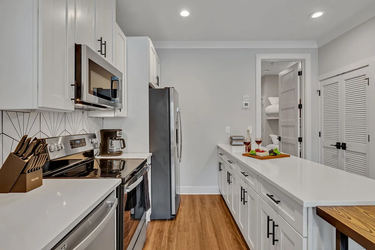 This image showcases a contemporary kitchen with stainless steel appliances, white cabinetry, and a geometric backsplash. The kitchen island features a serving tray, suggesting both meal prep and casual dining possibilities.
