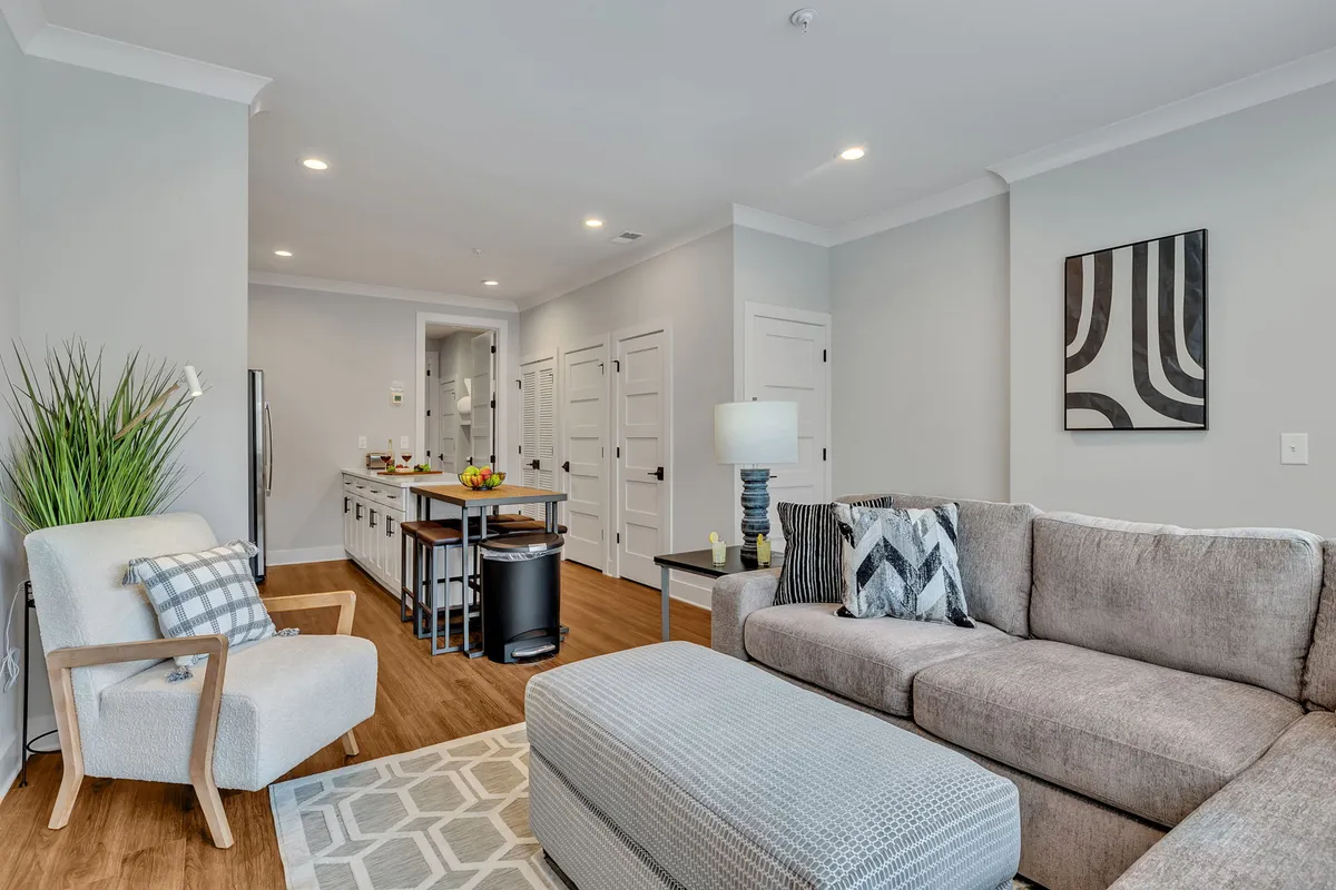 The image showcases a cozy, open-concept living space with a plush sofa, an inviting ottoman, contemporary kitchen area, and stylish artwork adorning the wall. The atmosphere is warm and welcoming, perfect for gathering with friends or unwinding after a day exploring Nashville.