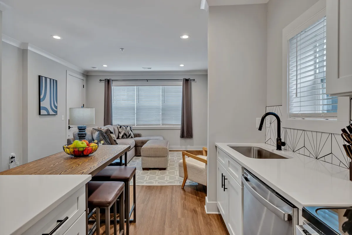A wide-angle view of the open-concept living space, blending the kitchen island, a comfortable living room sofa, decorative artwork, and a window with curtains, creating a sense of spaciousness and togetherness.