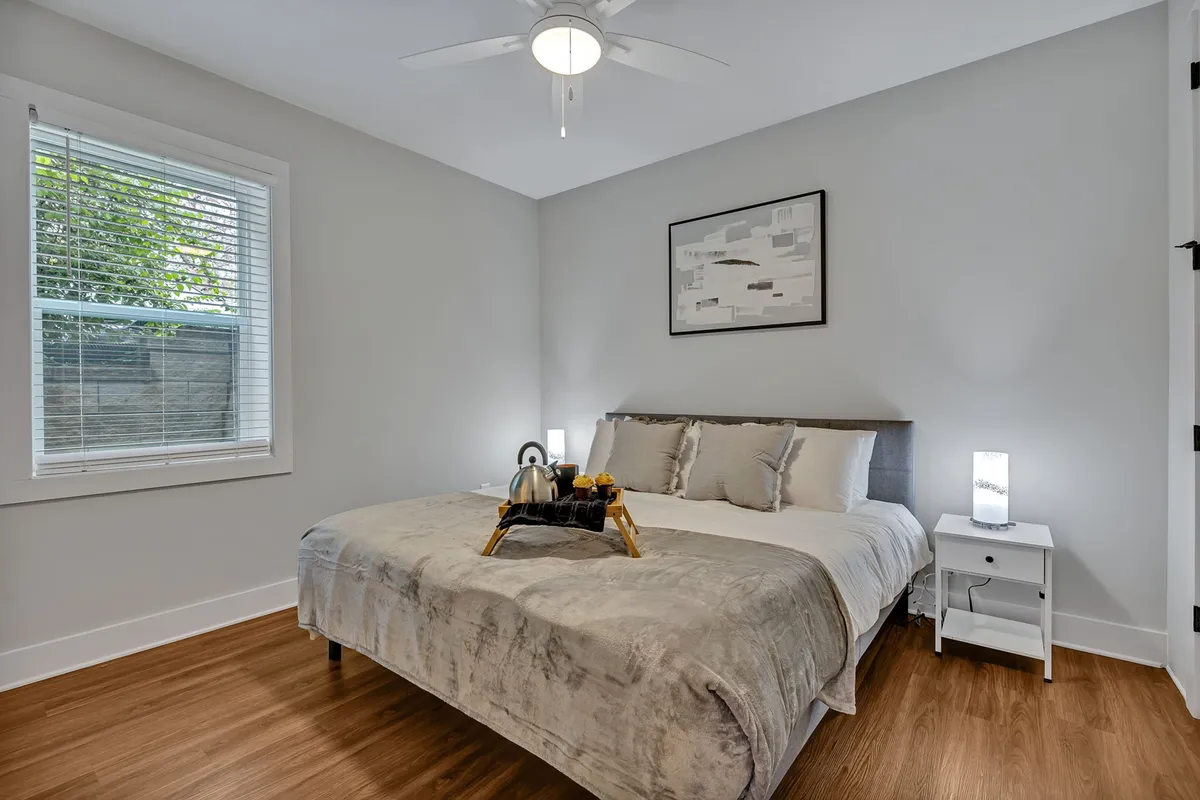 A serene bedroom features a plush king bed adorned with decorative pillows, a tray holding a teapot and fresh fruit, and tasteful artwork on the wall. The overall ambiance is tranquil and inviting, suggesting a restful retreat after a day of exploration.